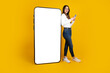 Full length body view woman leaning standing near big huge blank screen mobile cell phone with mockup using smartphone  on her hand. Looking camera, smiling happy girl. Banner design concept image.