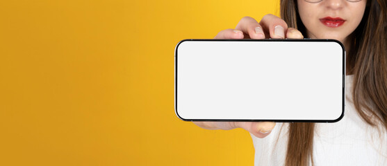 Horizontal smartphone mockup, unrecognizable woman showing horizontal smartphone mockup. Modern mobile phone with empty blank white screen. Banner design template with yellow background, copy space.