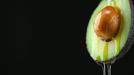 Canvas Print - Avocado oil pouring, dripping essential oil on cut avocado isolated on black background, slow motion. Fresh cut avocado with oil stream. Concept of healthy fruit for eating or cosmetics. 