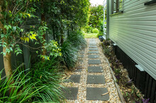 A Landscaped Side Garden Space With A Variety Of Plants And Trees Of A Typical Weather Board Home In Queensland Australia. Narrow Area With Stepping Stone Walkway Or Pathway Between Suburban Houses.