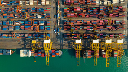 Wall Mural - commercial port loading and unloading cargo from container ship import and export by crane for distributing goods by trailers transported to customers and dealers, aerial top view.