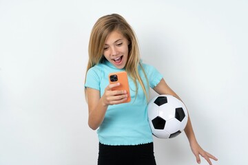 Wall Mural - beautiful caucasian teen girl wearing sportswear holding a football ball over white wall holding in hands cell reading browsing news