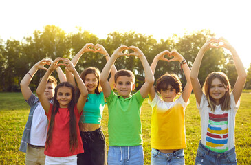 Happy children wish for world peace. Cheerful healthy kids standing on camp field or park lawn in sunset or sunrise sunlight look at camera, smile, raise hands up and do heart gestures. Group portrait