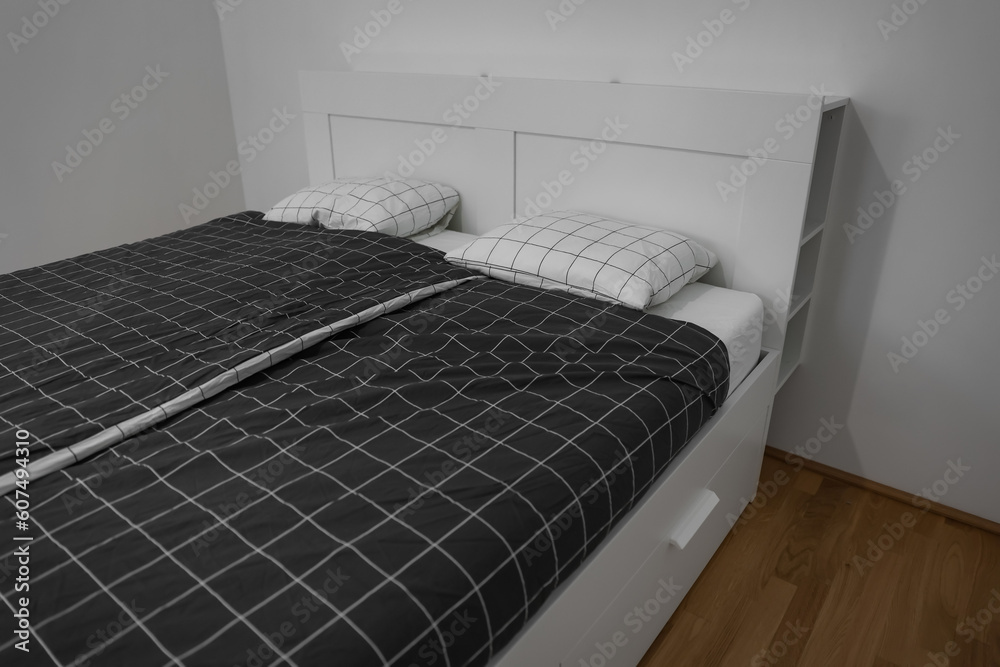 Modern bed with pillows near light wall