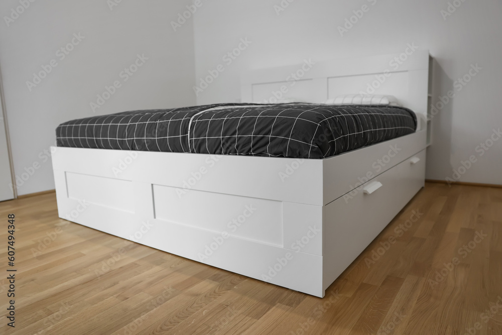 Modern bed with pillows near light wall