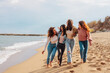 Four young diverse women having fun while walking on beach