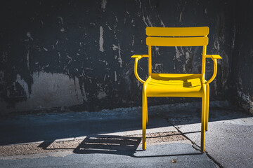 Yellow modern garden chair in front of old concrete wall, high contrasts of sun and shadow, modern urban concept