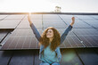 © Halfpoint - Portrait of young excited woman on roof with solar panels.