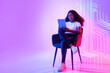canvas print picture - Online life. Young positive african american woman web surfing on digital tablet, sitting in armchair over neon light
