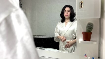 video of portrait of a young latin woman in robe in front of the mirror at home with her hands on he