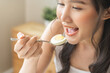 © KMPZZZ - Protein in food, happy smiling asian young woman, girl in diet eat boiled egg, hand holding spoon put food in mouth with for breakfast in the morning at home. Health care, loss weight people concept.