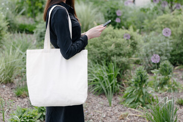 Woman holding white textile eco bag against urban city background. Ecology or environment protection concept. White eco bag for mock up.