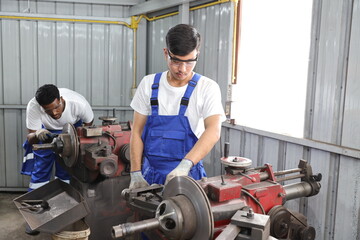 Multiethnic technicain mechanic or worker man in protective uniform using metal lathe machine operate polishing car disc brake at garage. Maintenance automotive and inspecting vehicle part concept