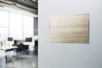 Blank wooden printed poster with place for your logo or text on light grey wall background in modern office area with blurred furniture on background. 3D rendering, mockup