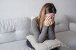 © Julija - Young depressed woman sitting on sofa in living room. She feeling sad and worried suffering depression in mental health.