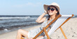 © rogerphoto - Happy brunette woman wearing sunglasses and hat relaxing on a wooden deck chair at the ocean beach.