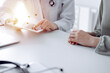 © rogerphoto - Doctor and patient sitting at the desk in clinic office. The focus is on female physician's hands using tablet computer, close up. Medicine concept.