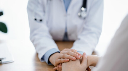 Doctor and patient sitting at the wooden table in clinic. Female physician's hands reassuring woman. Medicine concept.