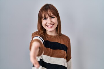 Poster - Young beautiful woman wearing striped sweater over isolated background smiling friendly offering handshake as greeting and welcoming. successful business.