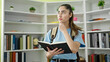 © Krakenimages.com - Young beautiful hispanic woman student reading book standing with doubt expression at library university