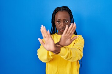 Wall Mural - Beautiful black woman standing over blue background rejection expression crossing arms and palms doing negative sign, angry face