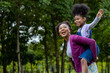 © Akarawut - African American mother is playing piggyback riding with her young daughter while having a summer picnic in the public park for wellbeing and happiness concept