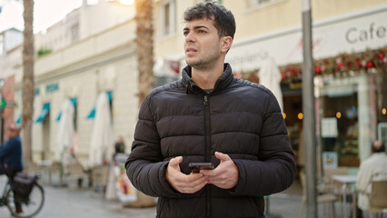 Canvas Print - Young hispanic man using smartphone looking away at coffee shop terrace