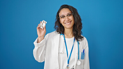 Sticker - Young beautiful hispanic woman doctor holding pills over isolated blue wall background