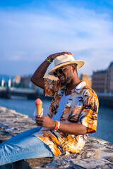 Wall Mural - Black ethnic man enjoy summer vacation at the beach eating ice cream, sitting by the river