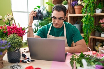 Sticker - Young hispanic man florist holding professional camera using laptop at flower shop