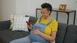 Young pregnant woman using smartphone sitting on sofa at home