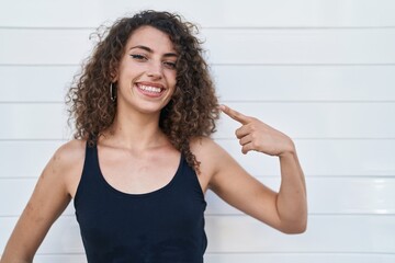 Sticker - Hispanic woman with curly hair standing over white background smiling happy pointing with hand and finger