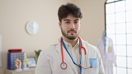 Poster - Young hispanic man doctor standing with serious expression at clinic