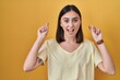 © Krakenimages.com - Hispanic girl wearing casual t shirt over yellow background smiling amazed and surprised and pointing up with fingers and raised arms.