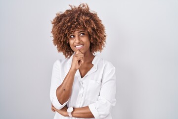 Sticker - Young hispanic woman with curly hair standing over white background with hand on chin thinking about question, pensive expression. smiling and thoughtful face. doubt concept.