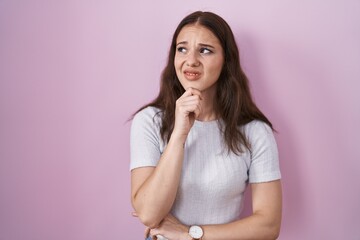 Poster - Young hispanic girl standing over pink background thinking worried about a question, concerned and nervous with hand on chin