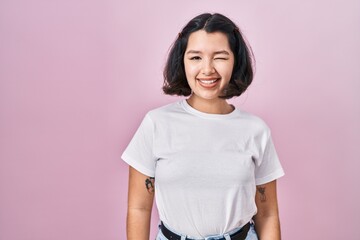 Sticker - Young hispanic woman wearing casual white t shirt over pink background winking looking at the camera with sexy expression, cheerful and happy face.