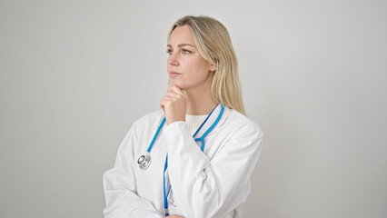 Wall Mural - Young blonde woman doctor standing with doubt expression thinking over isolated white background