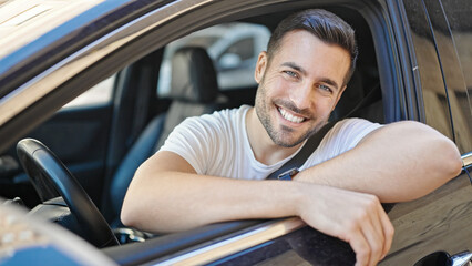 Canvas Print - Young hispanic man smiling confident sitting on car at street