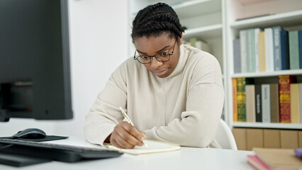 Canvas Print - African american woman student using computer writing notes at library university