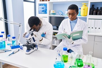 Canvas Print - Man and woman scientists using microscope writing on notebook at laboratory