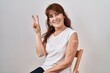 Middle age hispanic woman getting vaccine showing arm with band aid smiling looking to the camera showing fingers doing victory sign. number two.