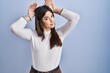 Young brunette woman standing over blue background doing bunny ears gesture with hands palms looking cynical and skeptical. easter rabbit concept.