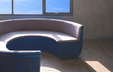 Wall Mural - Sunlight and shadow on surface of empty curved sofa near glass window on loft concrete wall in vintage living room