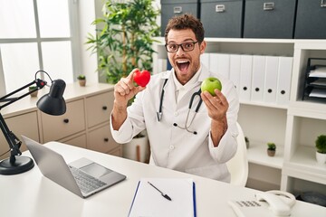 Canvas Print - Young hispanic man working at dietitian clinic celebrating crazy and amazed for success with open eyes screaming excited.