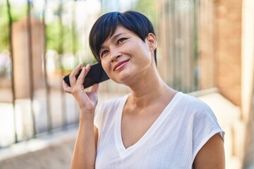 Poster - Middle age chinese woman smiling confident listening audio message by the smartphone at street