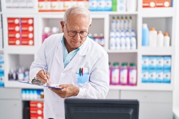 Canvas Print - Senior grey-haired man pharmacist writing on document at pharmacy