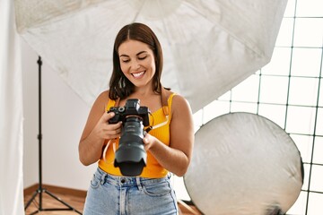 Sticker - Young beautiful hispanic woman photographer holding professional camera photo studio