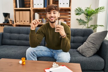 Poster - Arab man with beard working on depression holding pills and water smiling with a happy and cool smile on face. showing teeth.