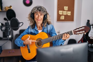 Wall Mural - Middle age woman playing classic guitar at music studio smiling happy pointing with hand and finger